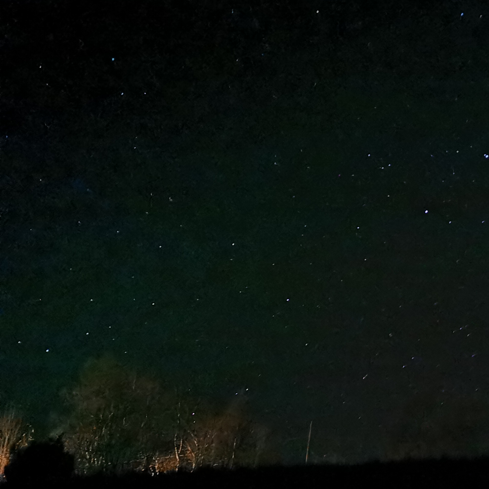 A dark night sky. Some trees and a field are barely visible in the foreground